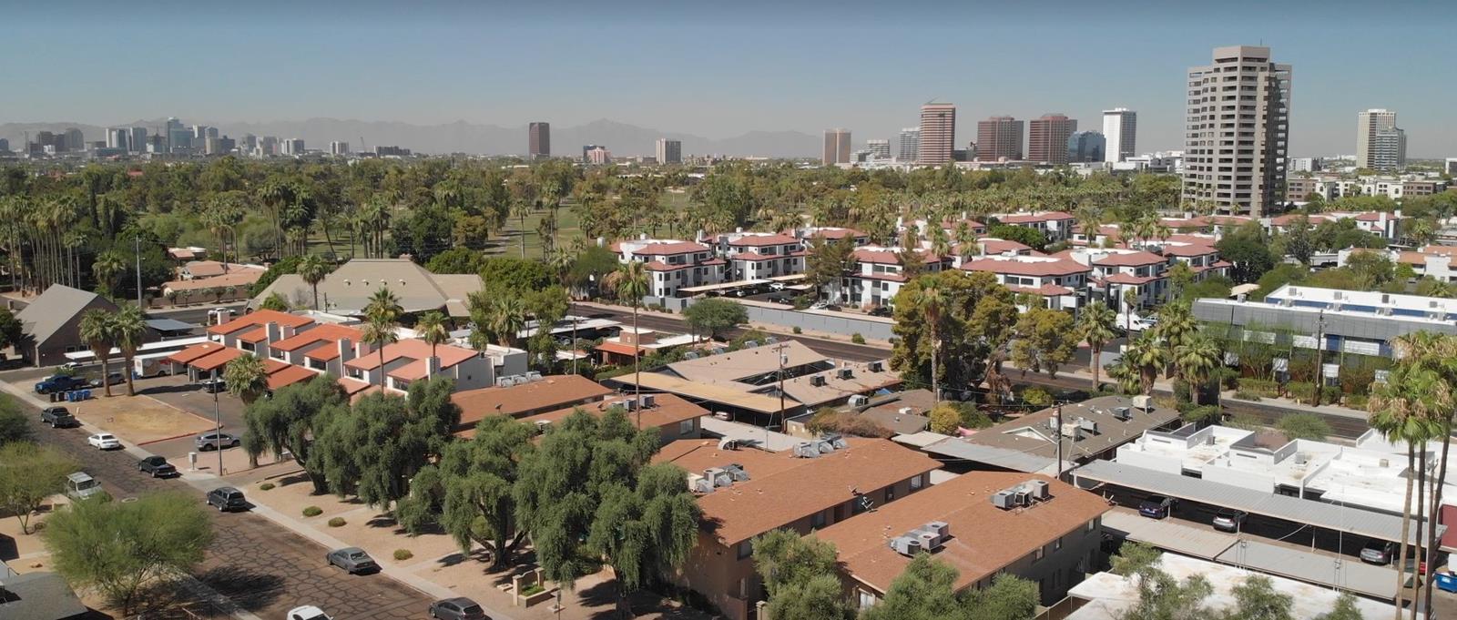 Aerial view of a Phoenix neighborhood with multifamily apartment communities, palm trees, and the downtown skyline on the horizon